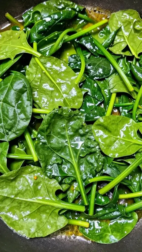 Closeup sautéed spinach leaves shimmering in buttered pan edge