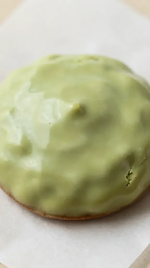 Closeup of a single glossy matcha white chocolate cookie on parchment